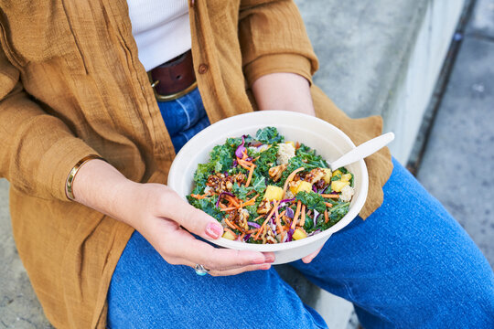woman eats salad outdoors focus on hands holding bowl