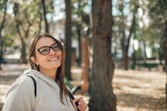 portrait of a young beautiful smiling caucasian woman. In a city autumn park, a woman with glasses in a light sweater. street photo