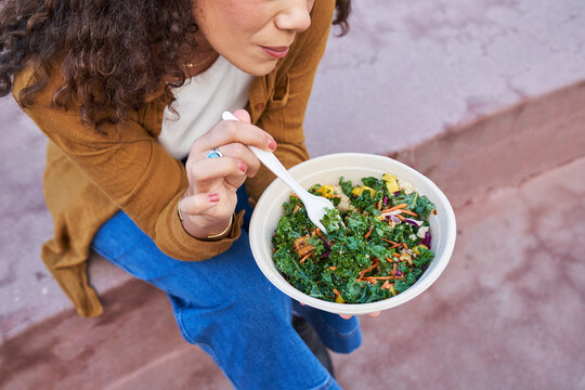 woman eats salad outdoors partial face focus on salad 