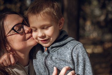 mother lovingly hugs and kisses her beloved son. in a city autumn park Woman with glasses