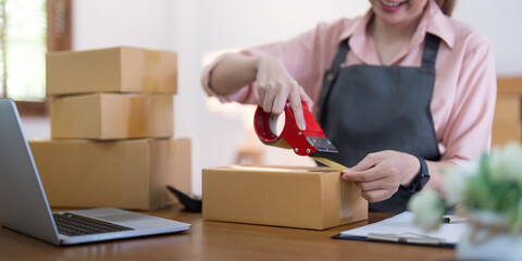 Woman use scotch tape to attach parcel boxes to prepare goods for the process of packaging,...