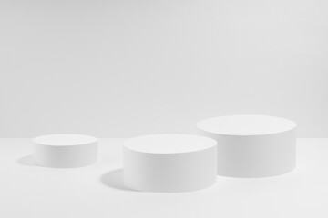White abstract stage mockup with  three white round podiums for cosmetic products in hard light on white background. Scene for presentation cosmetic products, gifts, goods, advertising, design, sale.