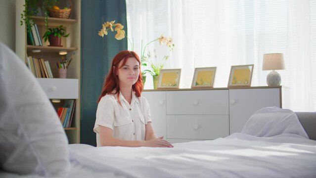 portrait of young woman while cleaning bed after sleep in a cozy room, smiling and looking at camera