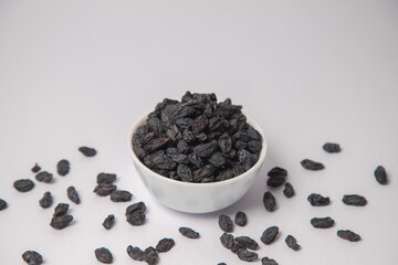 Dried black raisin on white bowl with white background, Dried black raisin scattered on the white background in a black bowl or vessel. Difference between seed and seedless black raisins