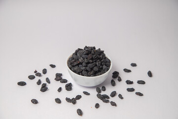 Dried black raisin on white bowl with white background, Dried black raisin scattered on the white background in a black bowl or vessel. Difference between seed and seedless black raisins