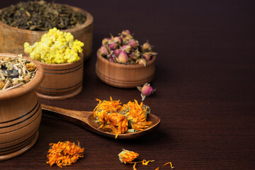 Various dried tea leaves in wooden bowl and spoon. Different dry herbs and flowers for making healthy tea background. Side view,space for text.
