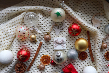 Various colorful Christmas ornaments, small presents and seasonal spices on white knitted blanket. Top view.