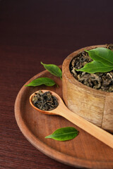 Dry tea with green leaves in wooden bowl and spoon on dark wooden table. Medicinal herbal collection. Banner. Side view.
