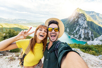 Happy couple taking selfie pic with smart mobile phone on top of the mountain - Young hikers climbing the cliff - Sport, technology and travel life style concept - obrazy, fototapety, plakaty