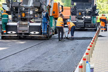A team of road workers with asphalt pavers lay down fresh asphalt on a city street on a summer day. - 681464602