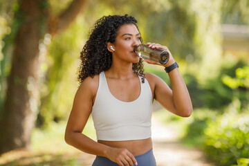 Young sporty woman sipping water training in sunny park outdoors