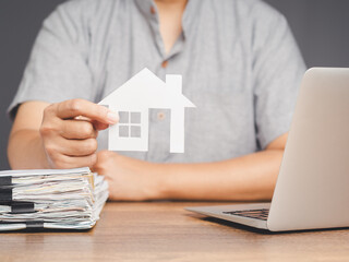 Fototapeta premium Businessman holding a mini paper house symbol while sitting at the desk