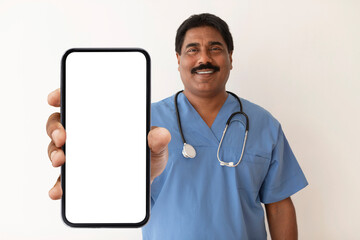 Indian Doctor Man Wearing Blue Scrubs Showing Big Smartphone With Blank Screen