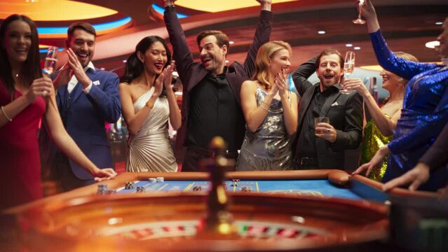 Successful Men and Women Partying in a Luxurious Casino. Young People Gambling at a Roulette Table, Gamblers Excited with Hitting the Jackpot and Winning a Big Sum of Money. Slow Motion Footage