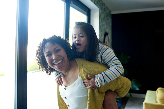 Happy mother with daughter with down syndrome playing in living room piggy back
