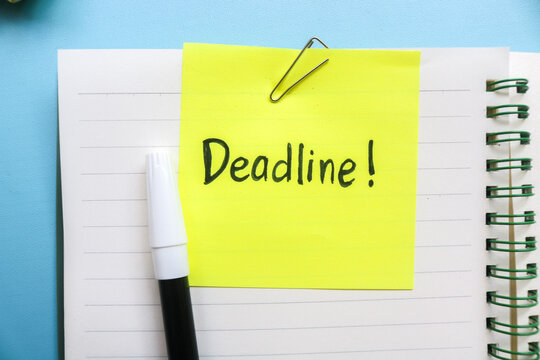 The word deadline written on a yellow memo sticky note on top of a notebook and isolated on a blue background with other objects such as pen, paper clip, binder clip, crumpled paper, sticky note