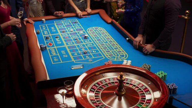 High Angle Footage of People Taking Risks and Placing Bets on a Roulette Wheel in a Casino. Croupier Placing a Ball into the Wheel, Focused on Table with Tokens, while Ball Spins on the Ball Track