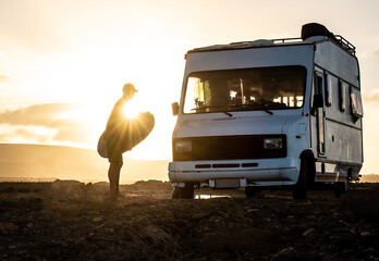 silhouette of person packing surf board on a motorhome sunset