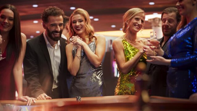 Successful Men and Women Partying in a Luxurious Casino Together. Young People Gambling at a Roulette Table, Gamblers Excited, Friends Talking with Each Other. Slow Motion Footage