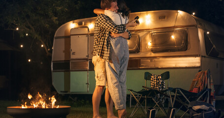Young Couple Hugging and Kissing Outdoors in a Camping Area with Caravans in the Evening After Boyfriend Making a Wedding proposal. Loving Partners Enjoy Spending Time and Traveling Together. - obrazy, fototapety, plakaty