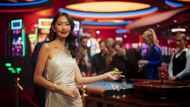 Portrait of a Beautiful Young Asian Woman Wearing an Elegant Silver Dress, Standing in a Modeling Pose and Gesturing at an Empty Space for Your Company Logo or Advertising Campaign Call to Action
