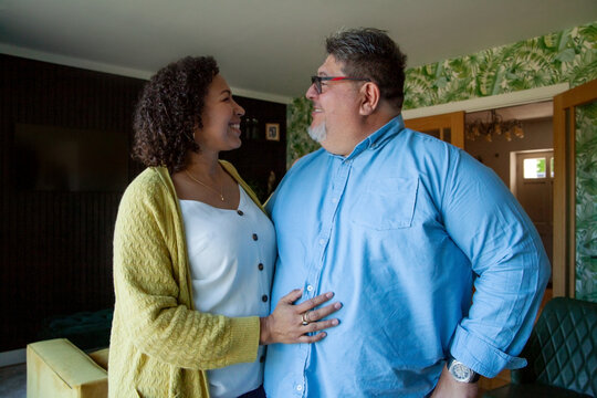 Body positive parents smiling at each other in the living room