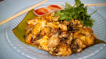 Chinese Oyster Omelette topped with sauce closeup, Hot pan of crispy fried oyster omelette served with bean sprout and spicy sauce.