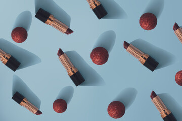 Obraz premium New Year pattern made with golden lipstick and red Xmas bauble on a bright blue background. Minimal Party, New Year's Eve concept. Flat lay.