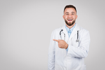 Joyful young male doctor pointing to the side at free space
