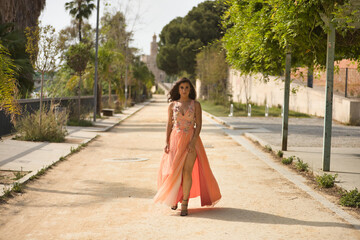 Young woman, Hispanic, beautiful, brunette, with an elegant salmon-colored dress, independent and empowered, lonely and strong walking down the street. Concept of beauty, fashion, trend, elegance.