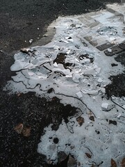 Broken asphalt road with pieces of ice and fallen leaves in winter