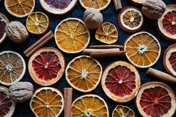 Dry orange and grapefruit slices next to cinnamon and walnuts on a dark background