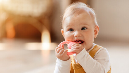 Closeup of cute little baby sitting on floor, chewing teether