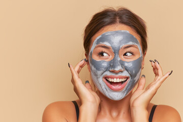 Closeup shot of smiling woman isolated over capuchino background with clay facial mask, skincare concept, copy space