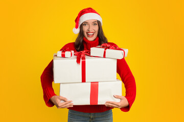 lady in Santa hat holds many Xmas gifts, yellow background