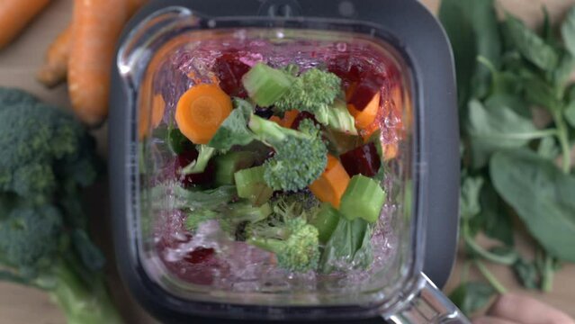 Veggies inside blender being mixed in super slow-motion at 800 fps captured with a high speed camera. Top view angle of blending broccolis, carrots, beets, leefs, celery with juicer