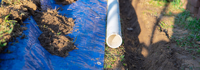 Panorama view plastic sewage pipes PVC, blue tarp with dirt, black mixing tub, pipe ready to...