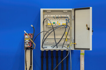 Electrical panel with protruding wires. Unfinished power cabinet. Electrical panel on blue wall. Metal cabinet with high-voltage cable protruding. Highly loaded electrical equipment.