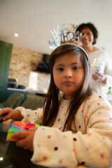 Little girl with down syndrome wearing tiara opening birthday presents and looking into camera © Anna Neubauer