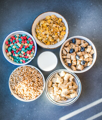 Variety of breakfast whole grain cereals and muesli in bowls on a light wooden background. Fast food. Top view. Space for text.
