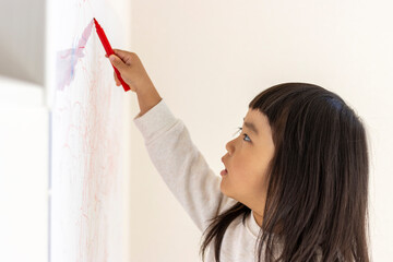 壁のホワイトボードに落書きする女の子（3歳、日本人）