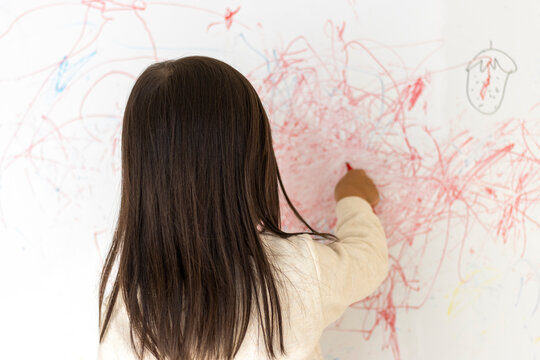 壁のホワイトボードに落書きする女の子の後ろ姿（3歳、日本人）