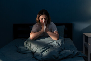 Beautiful woman suffering cold and flu trying to sleep at night, girl sneezing into a tissue in...