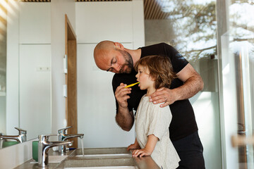 Father brushing son's teeth in bathroom