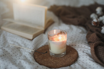 Cozy still life interior details with a book, candle and a cotton twig in warm soft bed. Sweet home