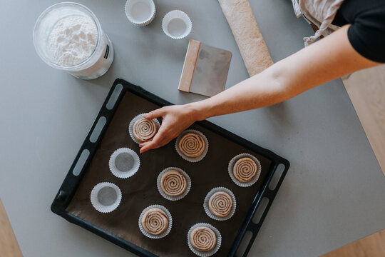 View of woman's hands putting raw cinnamon bun into cupcake case