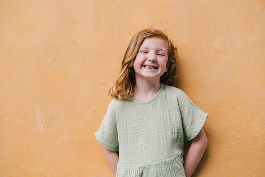 Red-haired girl smiling against wall