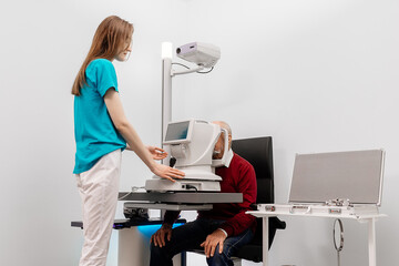 An elderly man undergoes an eye examination in a modern clinic. An expert checks vision using...