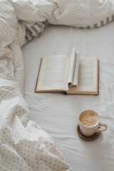 Fototapeta na wymiar Cozy morning composition with a coffee cup and a book with pages folded into a heart shape in bed