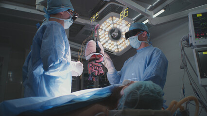 Doctors perform surgery in hospital operating room in VR headsets. 3D graphics of virtual...